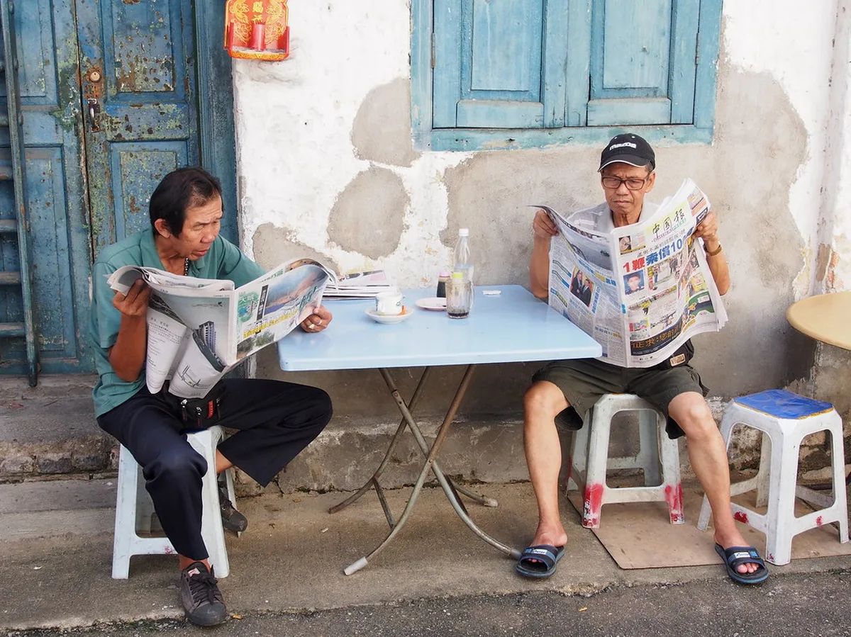 가게 앞 의자에 앉아 신문을 읽는 두 사람